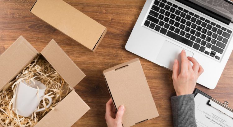 Lojista fazendo picking, ele está separando e embalando suas vendas com caixas de papelão ao lado de um notebook